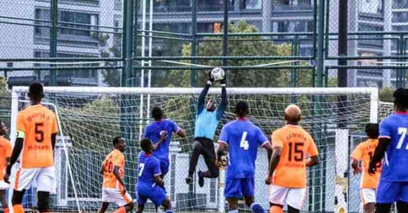 How Long Is A Soccer Match: A goalkeeper leaping to catch a soccer ball as players in orange and blue jerseys rush toward the goal in a vibrant urban setting.